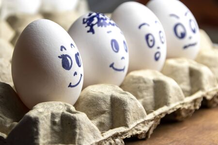 Lovely eggs in cardboard box. Eggs with emotions. White eggs in cardboard box with different faces...