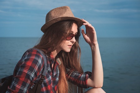 Close-up portrait of a beautiful young brunette girl in a hat and checkered red shirtagainst the sea on a sunny day.の写真素材