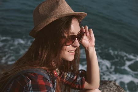 Close-up portrait of a beautiful young brunette girl in a hat and checkered red shirtagainst the sea on a sunny day.の写真素材