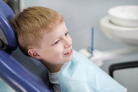 Male dentist examines the teeth of the patient cheerful child with blond hair. Boy smiling in dentists chair with mouth wide open.の写真素材
