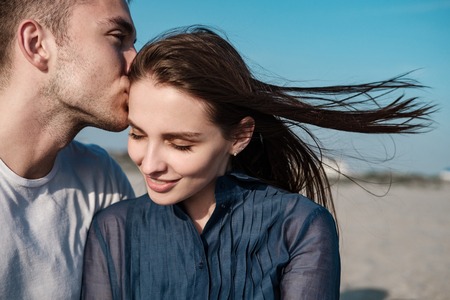 Beautiful couple, man and girl kissing and hugging on a sandy beach by the sea at sunset in sun glassesの写真素材