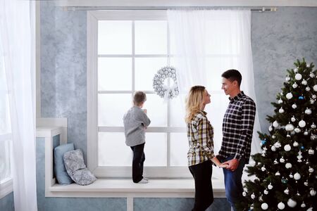 A family of three people exchanging New Years gifts sitting on the windowsill at the window with a Christmas treeの写真素材