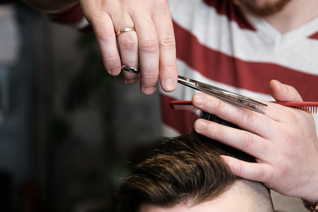 The hairdresser man in glasses cuts and shaves a beard to the young handsome man to the client in a...