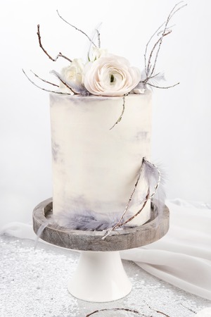 A white high wedding cake with pink and white flowers on top and on a wooden white stand, stands on a table with a white tablecloth.の写真素材