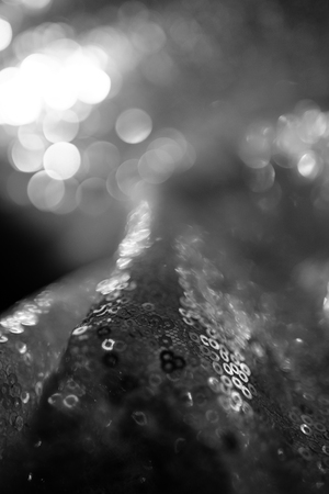 Smooth wawed tissue fabric folded on background. Colorless, gray, desaturated or black and white. Waves and creases on shiny flowing silk fabric. Circles bokeh in the defocus. Abstract forms of light.の写真素材