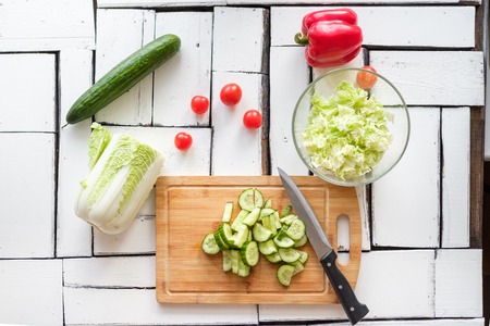 Vegetables salad, pepper, tomatoes and cucumber lie on a white table of wooden pieces on a bamboo-cut board. Food, breakfast, natural products.の写真素材
