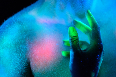 Young beautiful girl model with short haircut in the studio on a black background. Neon paints, makeup, body painting, colored hair coloring, creative color, poses in the light of soffits. Hands, face, blue, green, orange.の写真素材