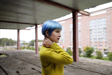 Beautiful girl model posing walks on a construction site at a height, second floor. A girl in a bright yellow sweater and a black leather skirt, blue hair and dark red lips.の写真素材