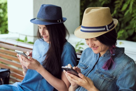 Two funny women friends laughing and sharing social media videos in a smart phone outdoorsの写真素材