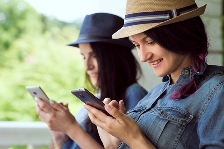Two funny women friends laughing and sharing social media videos in a smart phone outdoorsの写真素材