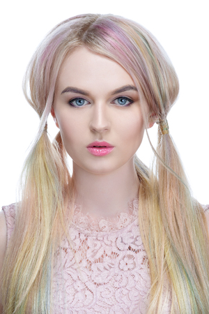 Beautiful girl model blonde with colored dyed hair and bright make-up, over white background licking candy striped lollipop. Work stylist hairdresser. Provocative view, Demonstration of sexuality.の写真素材