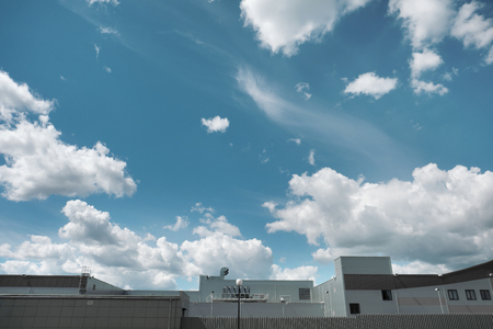 Top of the roof of a production metal building against a blue sky with clouds. Daylight aluminum frame and steel fence. Empty place for text.の写真素材