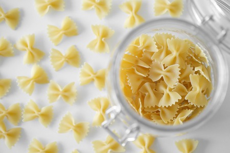 Uncooked Italian farfalle pasta, on a white background. Raw pasta is scattered around the trasparent...