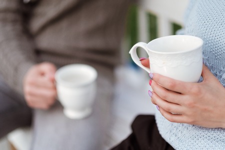 Friends, three people, a man and two women, drink tea and have a good time on the terrace of a country house. White curtains and cups.の写真素材