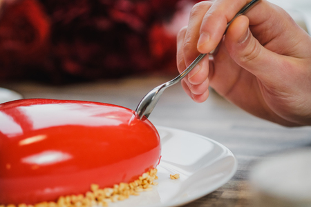 Red cake in the shape of a heart is on the table. Two hands with spoons, male and female, stretch into a pie. Romantic date, Valentine's Day.の写真素材