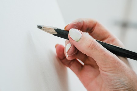 Woman artists hand with a large simple pencil, draws on a clean white canvas, close-up. Dirty nails, copy space.の写真素材