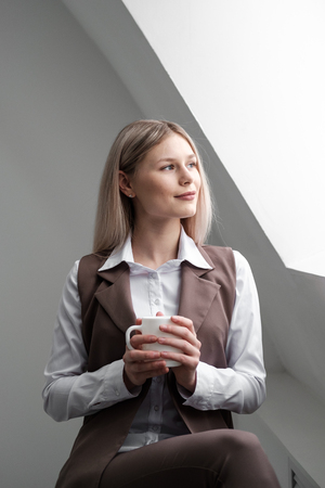 Blondina girl in a business suit sitting at a white table and working on a computer in a white bright office.の写真素材