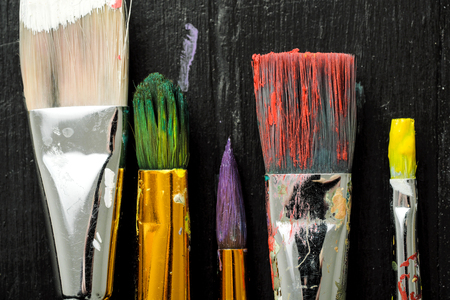 Artists tools, brushes in paint are in a row on a black wooden background. Abstract conceptual background.の写真素材