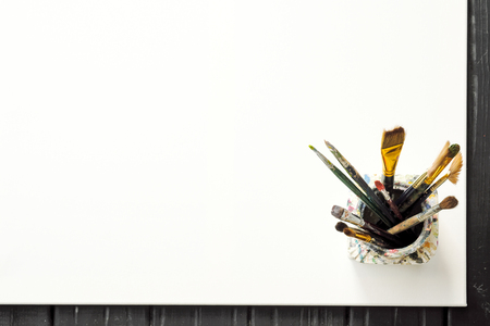 Artist's tools, brushes in paint are in the bank on a white canvas. Abstract conceptual background.の写真素材