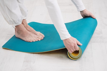 A male teacher and trainer in white clothes are laying out a yellow and blue yoga mat, preparing for a fitness class. The concept of the beginning of sports.の写真素材