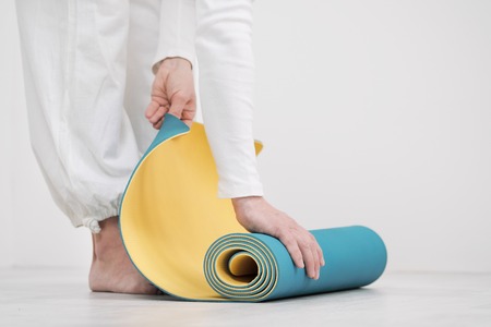 A male teacher and trainer in white clothes are laying out a yellow and blue yoga mat, preparing for a fitness class. The concept of the beginning of sports.の写真素材