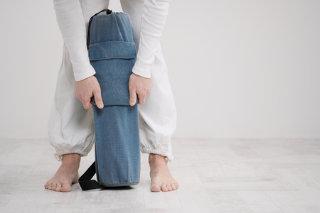 A male teacher and trainer in white clothes are laying out a yellow and blue yoga mat, preparing for a fitness class. The concept of the beginning of sports.の写真素材