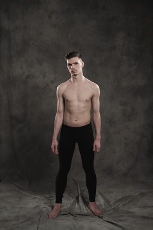 A young male ballet dancer with black leggings and a naked torso performs dance moves against a gray grunge background, with a light of lights and smoke. Conceptual art of contemporary.の写真素材