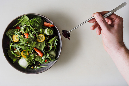 A male chef decorates a salad dish in a restaurant kitchen in a black apron. White cutting board, closeup of a hand with tongs.の写真素材
