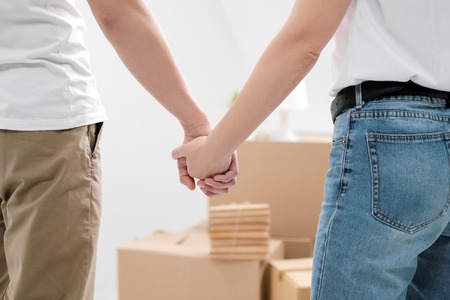 A man and a woman hold hands, against a background of cardboard boxes with things and a white background close-up. The concept of moving to a new home.の写真素材