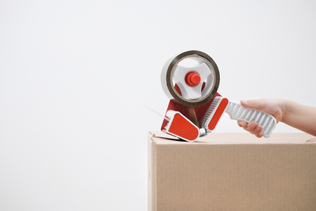 The hand of the child seals the cardboard boxes with a dispenser and adhesive tape. Concept themes moving to a new home.の写真素材