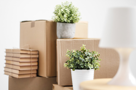 Cardboard boxes with things are stacked on the floor against the background of a white wall close up. Books and table lamps and green plants in pots. The concept of moving to a new home. Copy space.の写真素材