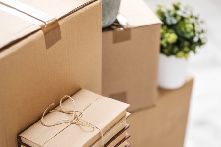 Cardboard boxes with things are stacked on the floor against the background of a white wall close up. Books and table lamps and green plants in pots. The concept of moving to a new home. Copy space.の写真素材