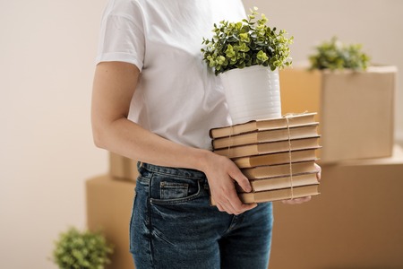 The concept of relocation and moving to a new home. Close-up, female hands hold a pile of books and...