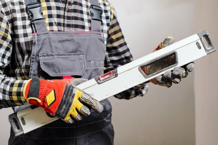Close-up of gloved hands of a builder and repairman with level. The concept of building and checking...
