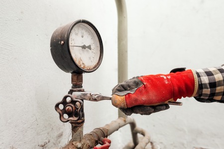 The technician with a wrench wrench turns the nut at the measuring device. The concept of repair and maintenance of measuring plumbing devices.の写真素材