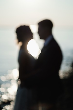 Loving couple at sunset. Blurred picture with glowing water background. Wedding and dating concept.の写真素材