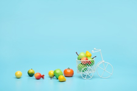 White wire bicycle with a basket filled with mini fruit. Near the bucket with vegetables and fruits. Blue background. Concept of harvesting and delivering fruits and vegetables, market.の写真素材