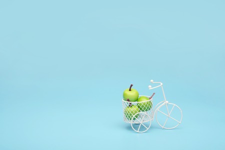 White wire bicycle with a basket filled with mini fruit. Near the bucket with vegetables and fruits. Blue background. Concept of harvesting and delivering fruits and vegetables, market.の写真素材