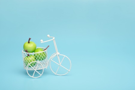 White wire bicycle with a basket filled with mini fruit. Near the bucket with vegetables and fruits. Blue background. Concept of harvesting and delivering fruits and vegetables, market.の写真素材