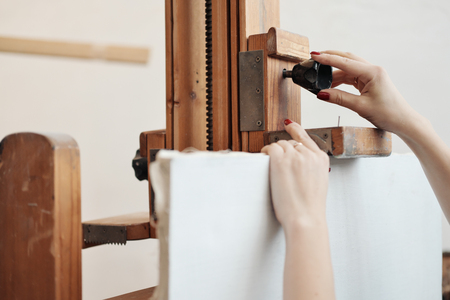 Woman artist fastens a canvas on a large wooden easel. The concept of the artist.の写真素材