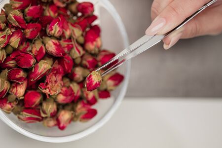 An attractive young female brunette confectioner decorates a white cake with small red flowers of food rose with tweezers. On a dark gray background.の写真素材