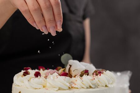 The condater sprinkles the cake with grated almonds and coconut. Close-up of a hand and pouring crumbs. White cake on a gray background.の写真素材