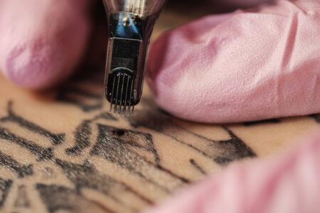 Close-up of a tattoo needle. The process of the tattoo master. Pink womens protective gloves. Tattoo sketch nun.の写真素材