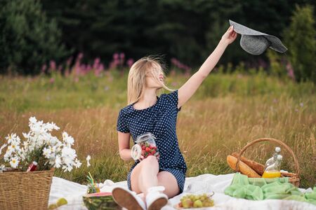 Young attractive woman in a blue dress at an outdoor picnic. A basket with daisies, watermelon, strawberries and a glass of lemonade. The concept of summer outdoor recreation.の写真素材