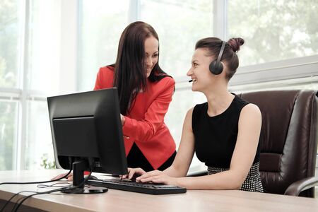 Two young women work in a bright office at the computer. Discuss workflows and enjoy a successful...