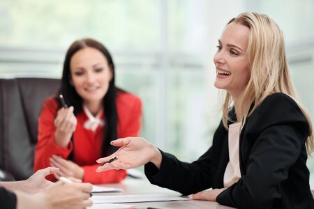 Three young attractive women in business suits are sitting at a desk and discussing workflows. Head...