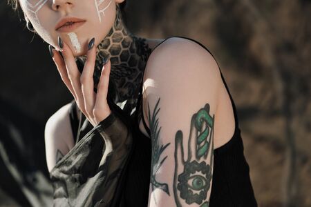 Beautiful sexy woman in black underwear. The body is covered with many tattoos. On the head dreadlocks. Posing against a sandy career and black fabric.の写真素材