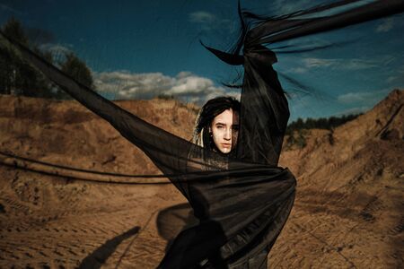 Beautiful sexy woman in black underwear. The body is covered with many tattoos. On the head dreadlocks. Posing against a sandy career and black fabric.の写真素材