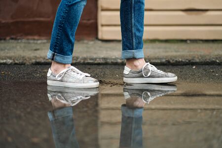 Close-up of feet in sneakers are walking through the puddles on the pavement. Rain and cloudy...