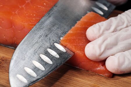 Hands cooks close-up. The chef cuts with a knife a red fish, smoked salmon on a wooden cutting...